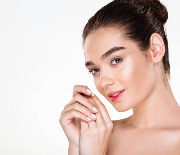 Horizontal portrait of beautiful young woman having fresh skin, posing over white background with hands together